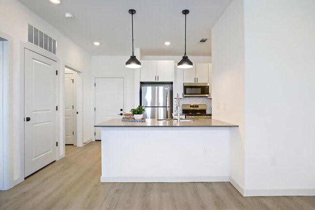The BH-A1 (L) floor plan includes a chef-ready kitchen with white shaker cabinets, herringbone tile backsplash, stainless steel appliances, and stylish pendant lighting. Garrett Harvest Junction West, Longmont, CO. - Garrett Harvest Junction West