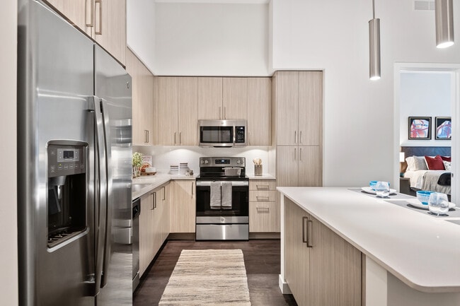 Cocina con gabinetes de roble, iluminación debajo de los gabinetes, encimeras de cuarzo blanco, electrodomésticos de acero inoxidable y pisos de tablones de vinilo de superficie dura. - Avalon Fort Lauderdale