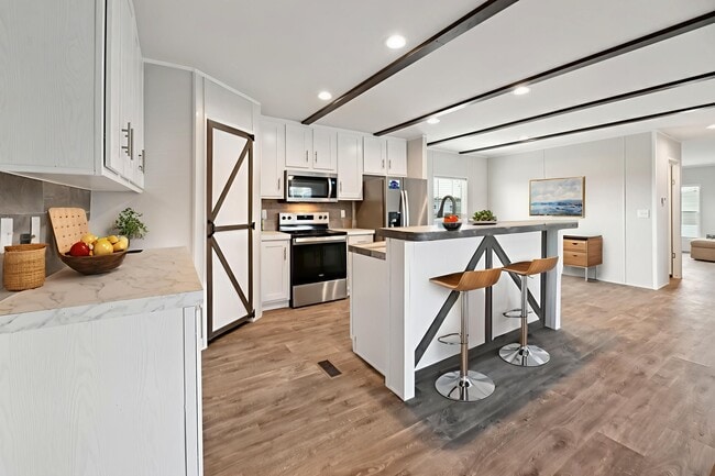 Cocina con gabinetes blancos, puerta estilo granero y barra de desayuno con dos taburetes de madera bajo lámparas colgantes.