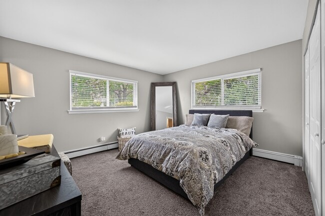 Rest easy in a comfortable bedroom featuring a nightstand and natural light at Renaissance at Carol Stream in Carol Stream, IL.