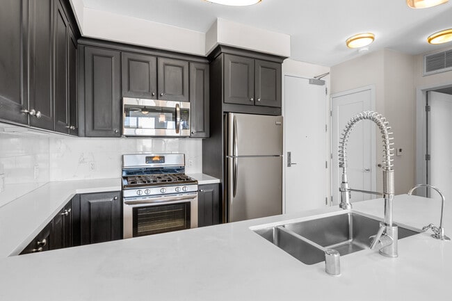 Kitchens with dark cabinetry, white quartz countertops, white tile backsplash, stainless steel appliances, and hard surface flooring