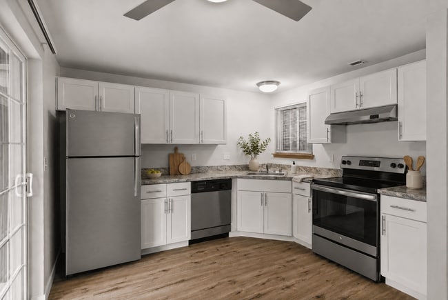 Staged apartment kitchen with white cabinetry, stainless-steel appliances, wood-look flooring, greenery, and modern countertop décor.