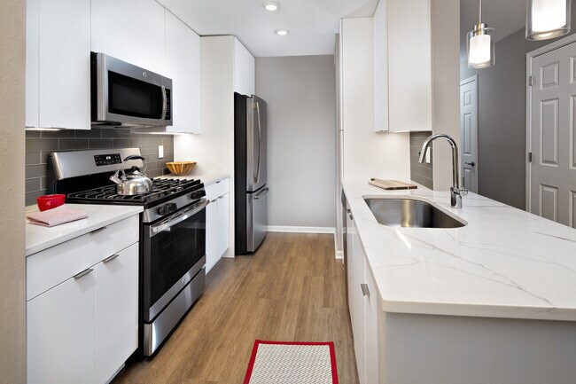 Premier Scheme kitchen with flat white cabinetry, white marbled quartz countertops, grey subway tile backsplash, stainless steel appliances, and hard surface flooring