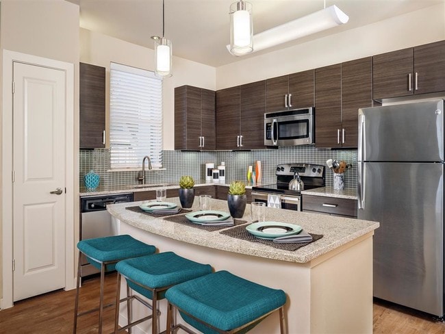 Kitchen with granite countertops, stainless steel appliances, wood-style floors, and modern lighting over island - Thirty Oaks Apartments