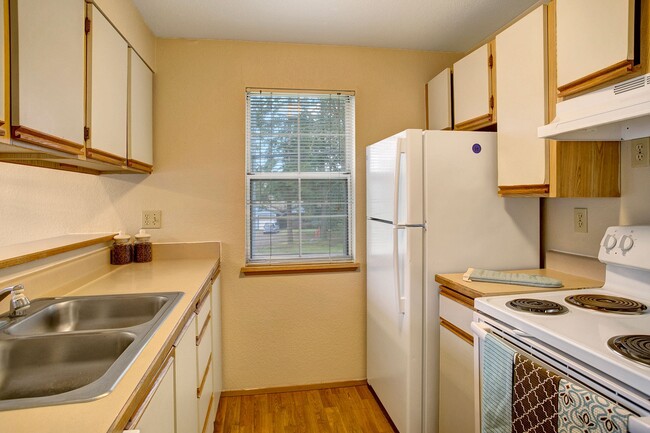 A kitchen with a window overlooking the property, lots of counter space, and plenty of cabinet storage space - Heron View Apartments