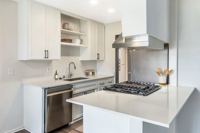 Renovated Package I kitchen with stainless steel appliances, white quartz countertops, white cabinetry, and hard surface flooring (select homes)