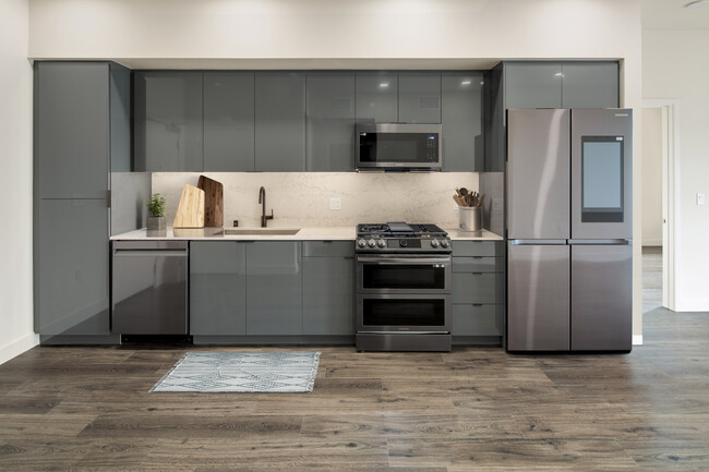 Upgrade Package Kitchen with grey cabinetry, undercabinet lighting, marble backsplash and countertop, and black stainless steel appliances - AVA Arts District Apartments