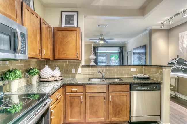 Kitchen with granite counter tops, stainless steel appliances, brown cabinetry. - Via Las Colinas