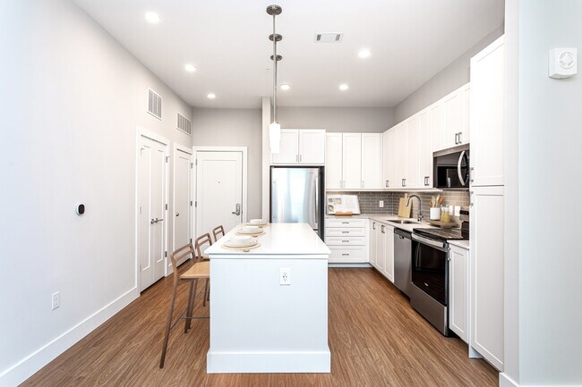 Modern kitchen with white cabinetry, undercabinet lighting, grey tile backsplash, and white quartz countertops - Avalon Carmel Commons