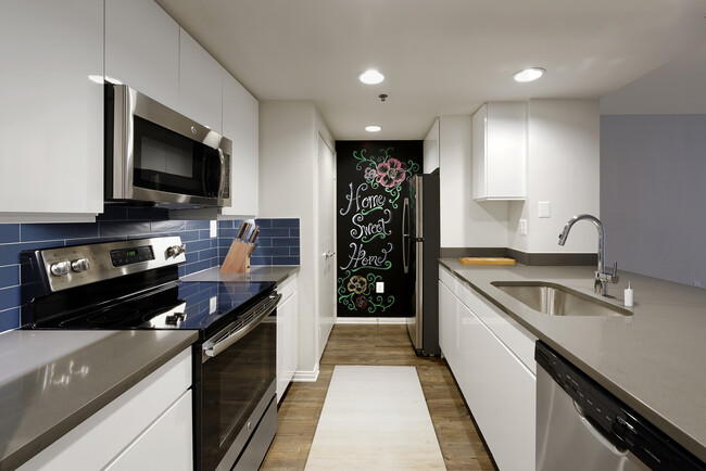 Renovated Package III kitchen with grey quartz countertops, blue tile backsplash, white cabinetry, stainless steel appliances, and hard surface plank flooring - AVA Ballston Square Apartments