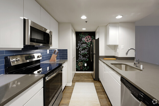 Renovated Package III kitchen with grey quartz countertops, blue tile backsplash, white cabinetry, stainless steel appliances, and hard surface plank flooring - AVA Ballston Square Rental