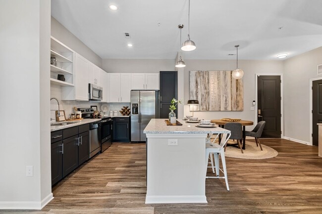 Cocina con gabinetes blancos y oscuros, encimeras de granito moteado, protector contra salpicaduras de azulejos blancos tipo metro, electrodomésticos de acero inoxidable y pisos de superficie dura. - Avalon at Palisades