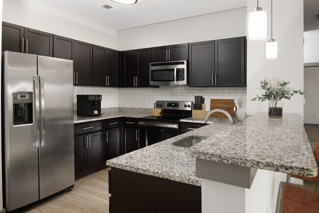 Renovated Package II Kitchen with dark cabinetry, speckled granite countertops, white tile backsplash, stainless steel appliances, pendant lighting, and hard surface flooring