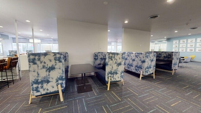 Moderna zona de estar con elegantes cabinas estampadas y elegantes mesas, perfecta para relajarse o celebrar reuniones informales en un ambiente vibrante. - University Plaza Apartments
