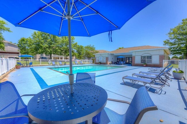 Outdoor pool with shaded table seating, lounge chairs, and clubhouse building framed by trees and fenced deck - Parham Pointe