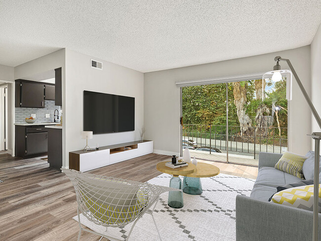 Hardwood floored living room with view of balcony and kitchen.