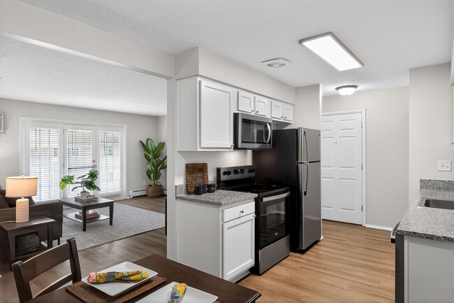 Moderna cocina y sala de estar de planta abierta con elegantes electrodomésticos de acero inoxidable, elegantes armarios blancos y abundante luz natural que entra por grandes ventanales con persianas. - University Oaks