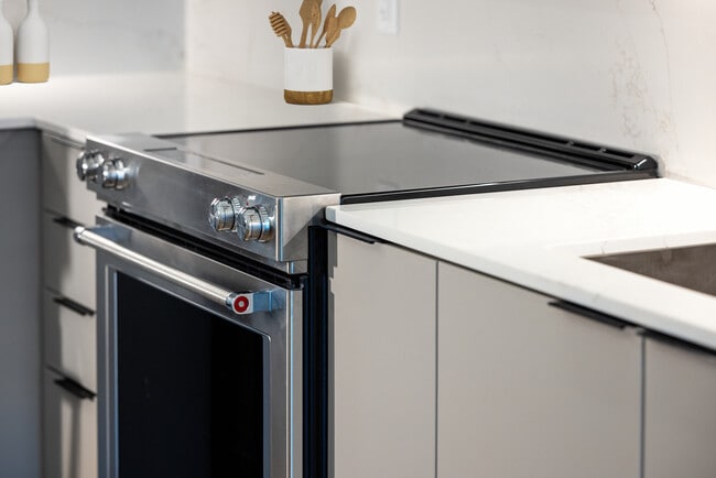 Signature Collection kitchen with light grey cabinetry, electric stove, and marbled quartz countertops and backsplash - Avalon at Becker Farm