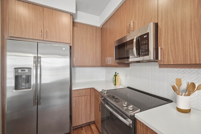 Cocina del paquete de acabados I con electrodomésticos de acero inoxidable, gabinetes oscuros, salpicadero de azulejos blancos y encimeras de cuarzo blanco.