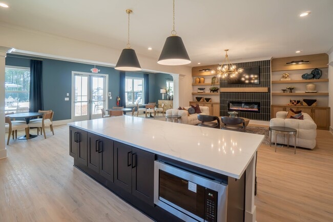 Kitchenette inside the Clubhouse with expansive island that offers bar seating and a microwave. Looking onto the living room area with ample seating, fireplace and TV.