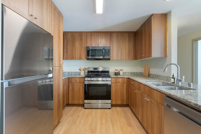 Renovated Package I kitchen with oak cabinetry, beige speckled granite countertops, stainless steel appliances, and hard surface flooring
