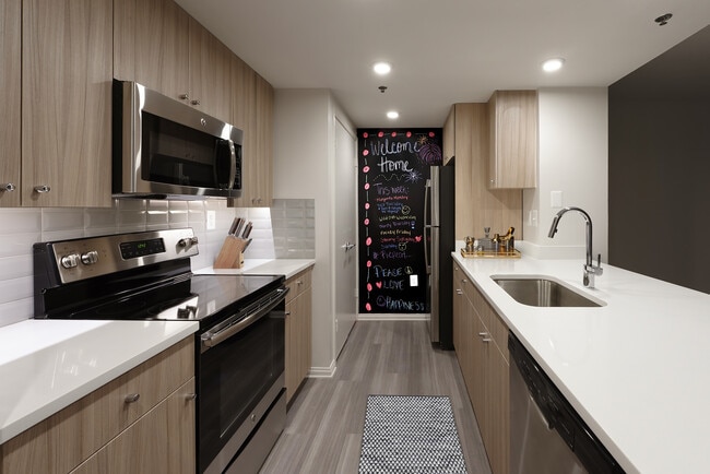 Cocina renovada del Paquete II con encimeras de cuarzo blanco, salpicadero de azulejos blancos, gabinetes de madera, electrodomésticos de acero inoxidable y pisos de madera de superficie dura