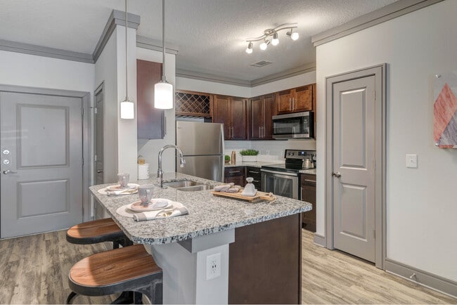 Modern kitchen with wood cabinetry, white tile backsplash, granite countertops, stainless steel appliances, and hard-surface flooring