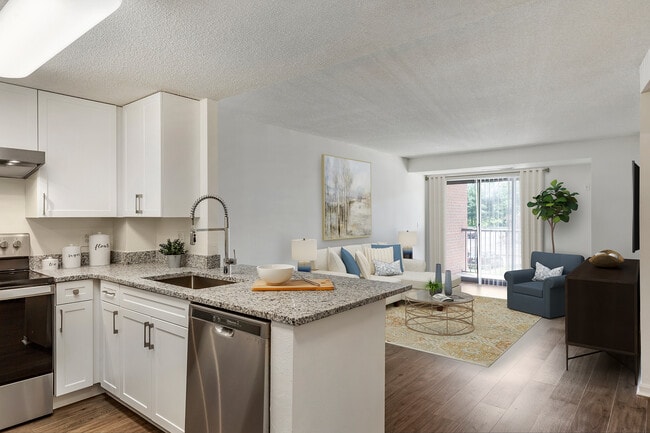 Renovated Package III kitchen and living area with white cabinetry, grey granite countertops, stainless steel appliances, and hard surface flooring