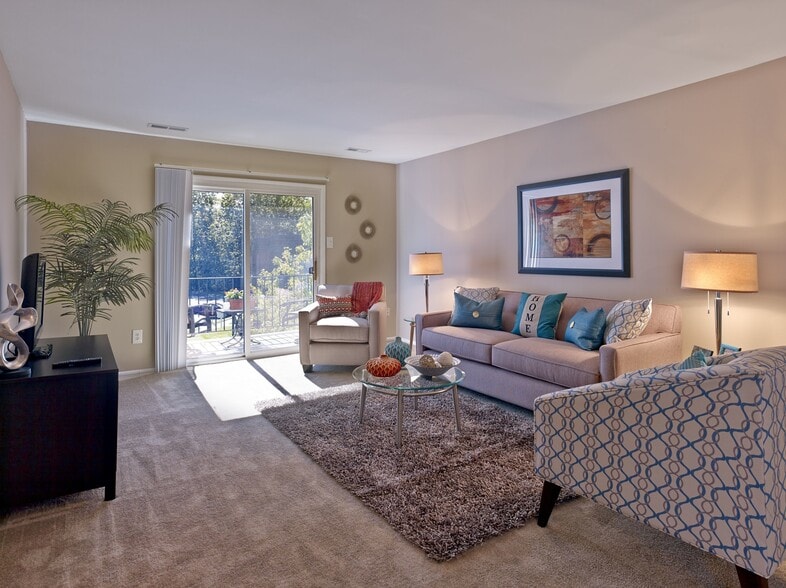 Enjoy a warm and inviting living room at Haynes Run Apartments, featuring plush carpeting, contemporary décor, and access to a private outdoor balcony.
