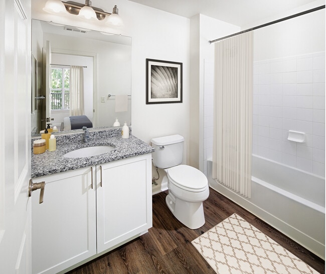 Phase I Renovated Package I apartment bath with grey speckled granite countertop, white cabinetry, and hard surface flooring