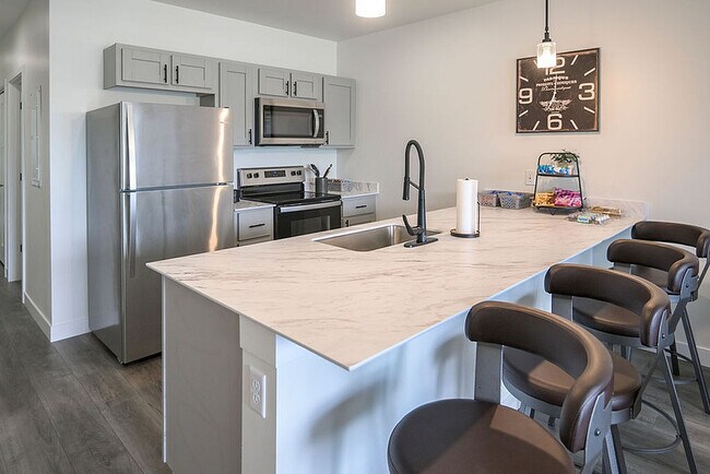 Modern kitchen with sleek stainless steel appliances, elegant marble countertop, and stylish bar seating. - Orchard on Wallen