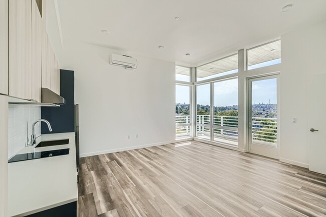 Experience the open layout of this modern kitchen and living room at Anker Ballard, featuring hardwood floors and a stunning city view.