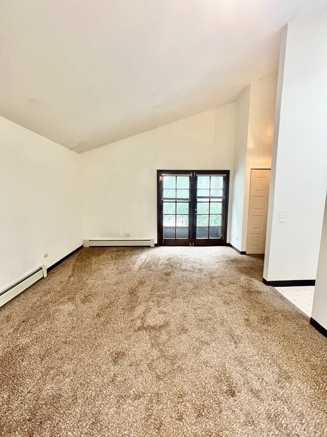 Bright and spacious living room with plush carpet and French doors leading to a serene outdoor view. - Char Rose