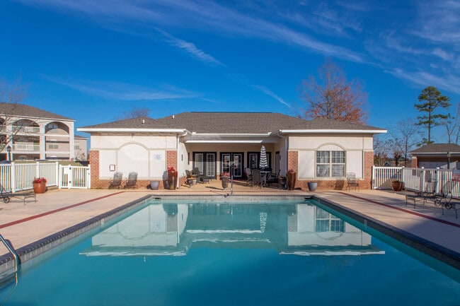 Ground level view of pool with calm water, surrounding deck seating, and clubhouse with covered patio and entry - Parham Pointe