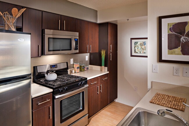 Classic Package I kitchen with espresso cabinetry, beige laminate countertops, stainless steel appliances, and hard surface plank flooring in select units