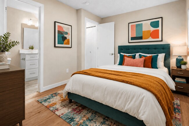 Un dormitorio elegante y confortable con detalles llamativos, suelo de madera cálida y fácil acceso al baño contiguo. - Crossroads at Meridian Apartments