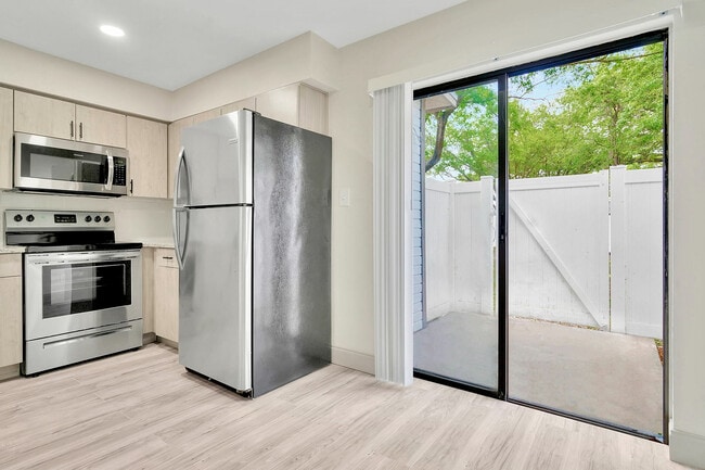 Chic modern kitchen with stainless steel appliances and bright sliding glass door leading to a private patio. - Temple Crest Townhomes