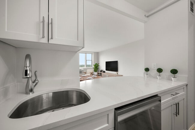 Modern kitchen with sleek stainless-steel appliances, statuario quartz countertops, and six burner gas stove, opening into a bright living area with a large window view at Parkside Place, apartments in Cambridge, MA