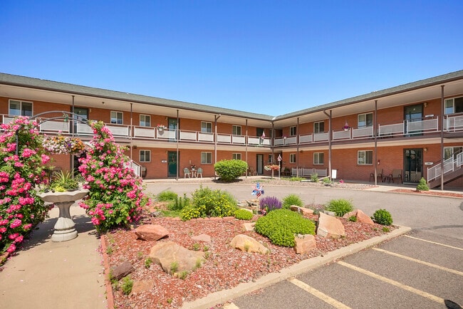 Charming apartment complex with well-maintained gardens and blooming flowers under a clear blue sky.