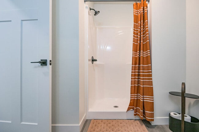 Baño luminoso con ducha moderna y elegante cortina de rayas naranjas, que ofrece un espacio refrescante.