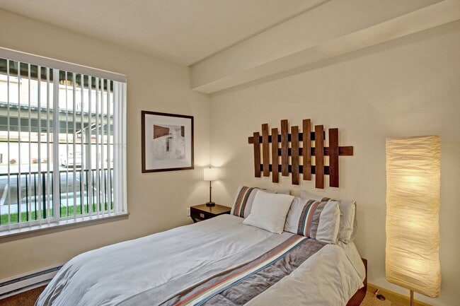 A bedroom with a bed and nightstand with a large window looking out to the property - Riverside 9