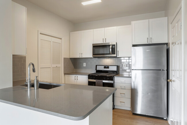 Renovated Package II kitchen with white cabinetry, grey quartz countertops, tile backsplash, stainless steel appliances, and hard surface flooring - Avalon Reston Landing Apartments