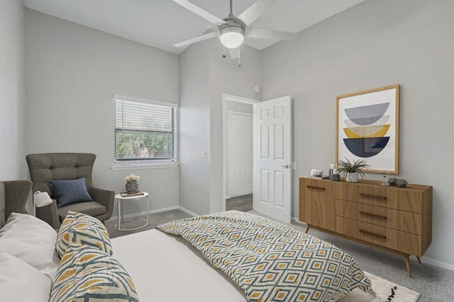 Bedroom with ceiling fan, patterned bedding, gray accent chair, wood dresser, framed wall art, and carpet flooring