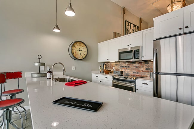 Modern kitchen with white cabinets and brick style backsplash, with white quartz countertop - Lofts at Mockingbird Station Apartments