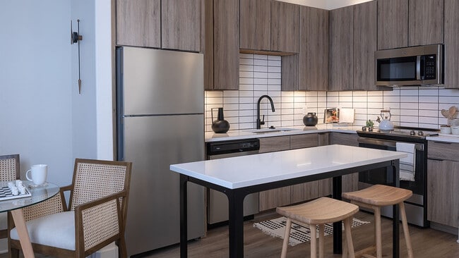 Cocina del apartamento con electrodomésticos de acero inoxidable, encimeras de cuarzo y suelos de madera.