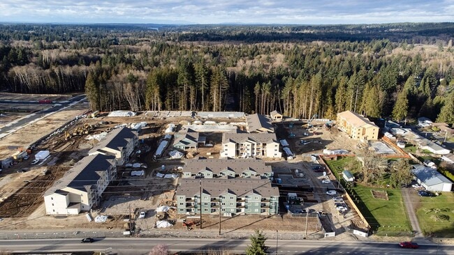 Wide aerial of construction at The Elowen in Lacey WA. New apartment homes taking shape among the towering evergreen trees on a bright Pacific Northwest day. - The Elowen