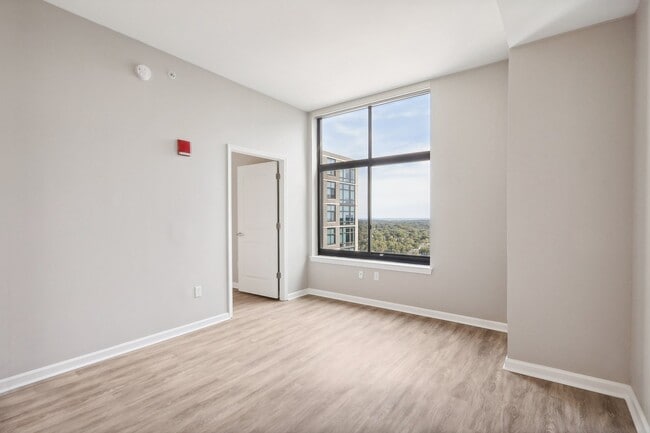 an empty living room with a large window and wood flooring - Arrive Wheaton