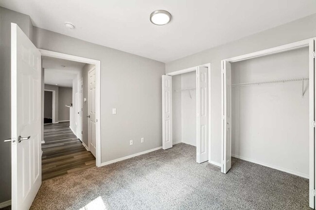 Bedroom with carpet flooring, neutral walls, dual closets with double doors, and open doorway leading to hallway space