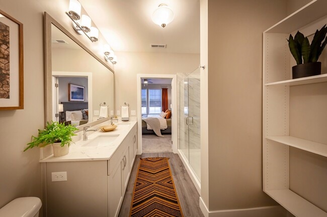 Modern apartment bathroom featuring elegant fixtures, a spacious vanity, glass-enclosed shower, and direct access to a private bedroom suite.