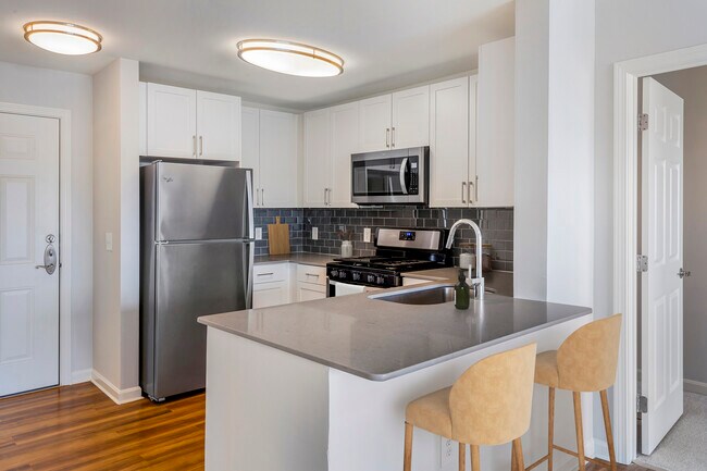 Renovated Package I kitchen with white cabinetry, grey quartz countertops, dark grey subway tile backsplash, stainless steel appliances, and hard surface flooring